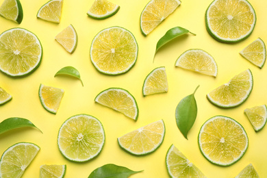 Photo of Juicy fresh lime slices and green leaves on yellow background, flat lay