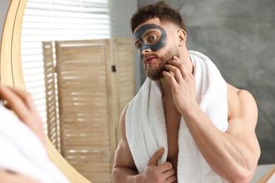 Handsome man with clay mask on his face near mirror in bathroom