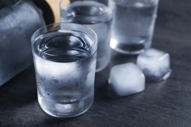 Photo of Shot glasses of vodka with ice on dark table, closeup