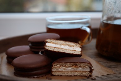 Photo of Tasty choco pies and tea on wooden tray, closeup view