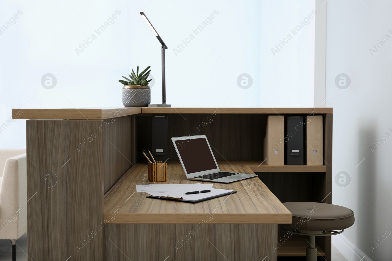 Photo of Stylish modern wooden desk with laptop indoors. Receptionist workplace