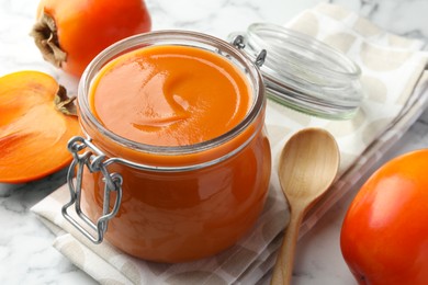 Delicious persimmon jam and fresh fruits on table, closeup