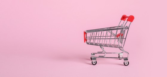 Photo of Small metal shopping cart on pink background, space for text