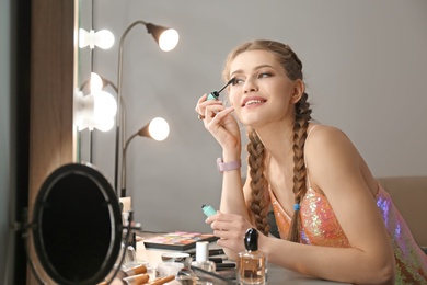 Photo of Portrait of beautiful woman applying makeup near mirror indoors