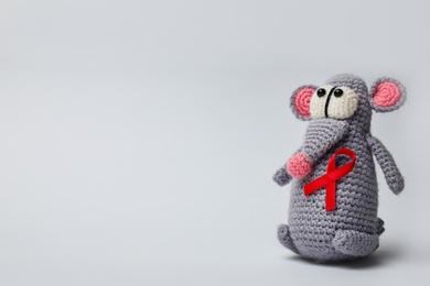 Photo of Cute knitted toy mouse with red ribbon on light grey background, space for text. AIDS disease awareness