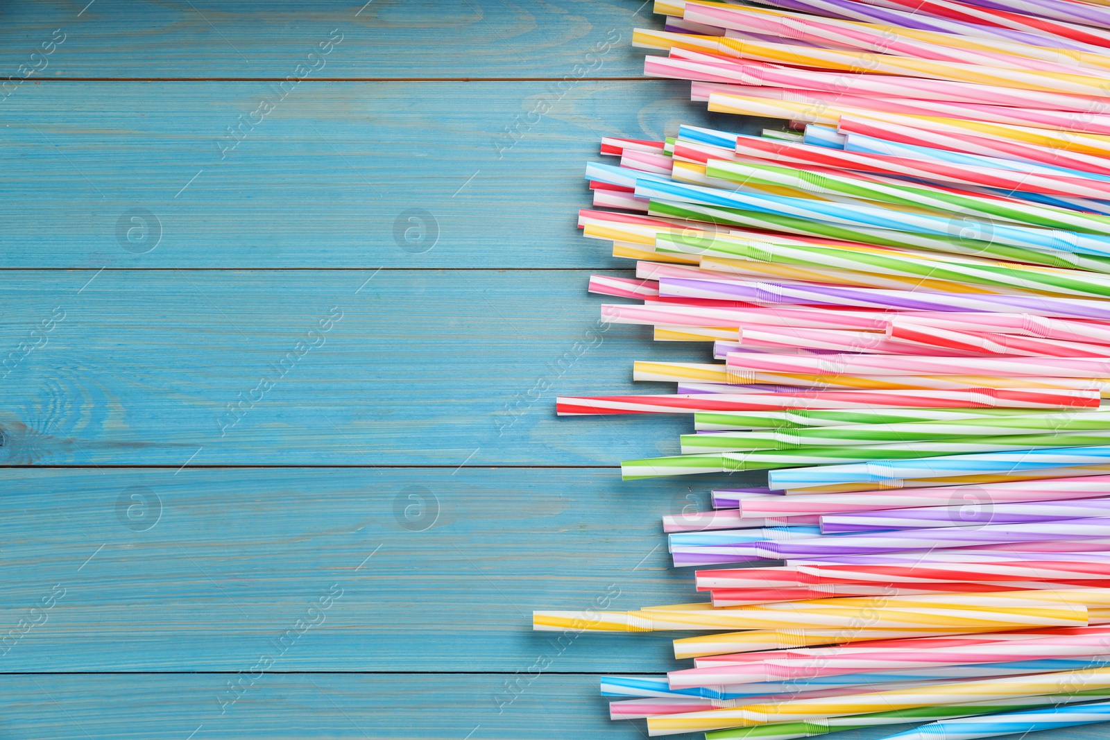 Photo of Colorful plastic drinking straws on light blue wooden table, flat lay. Space for text