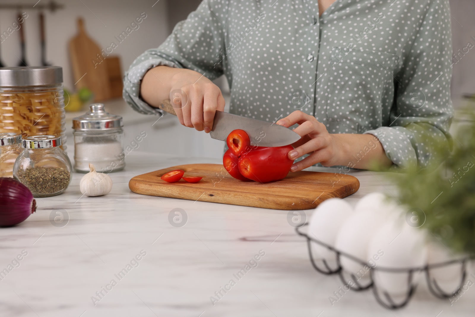 Photo of Cooking process. Woman cutting bell pepper at white countertop in kitchen, closeup