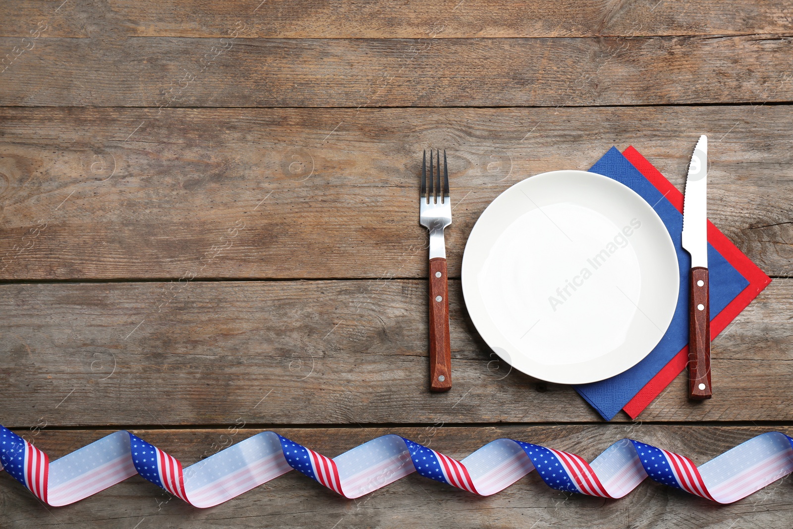 Photo of Patriotic table setting with traditional USA colors on wooden background, flat lay. Space for text