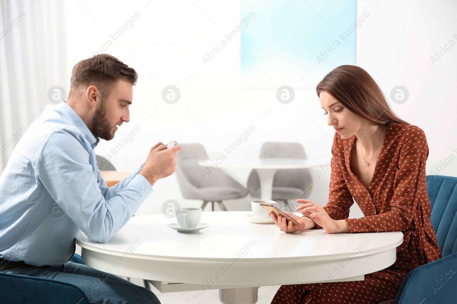 Photo of Couple addicted to smartphones ignoring each other in cafe. Relationship problems