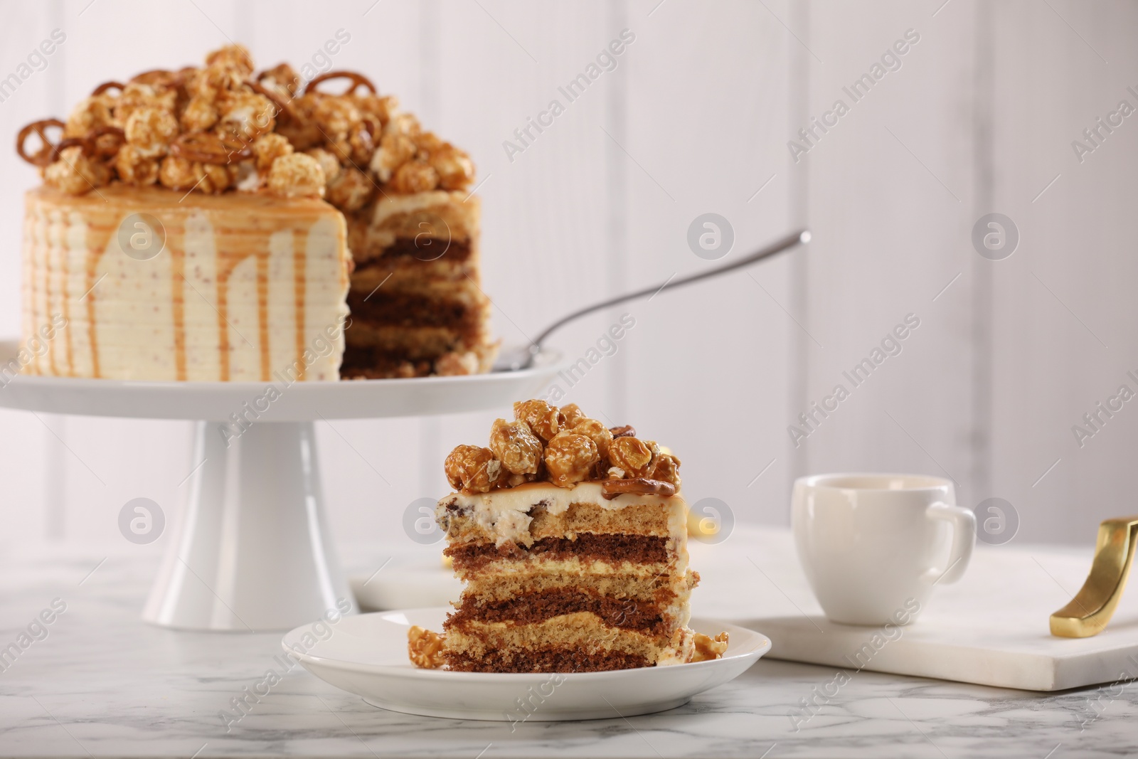 Photo of Piece of caramel drip cake decorated with popcorn and pretzels served on white marble table