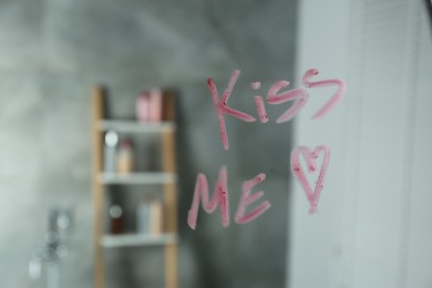 Photo of Red heart and phrase Kiss Me written with lipstick on mirror in bathroom, closeup