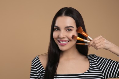 Happy woman with different makeup brushes on light brown background. Space for text