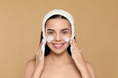 Happy young woman washing face with cosmetic product on beige background