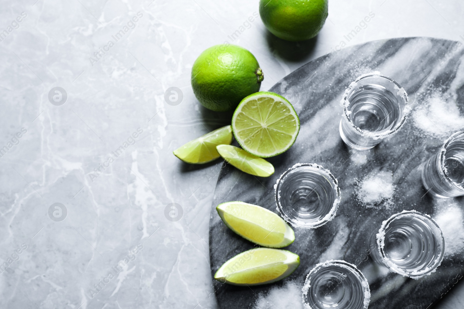 Photo of Mexican Tequila shots, lime slices and salt on grey marble table, flat lay. Space for text