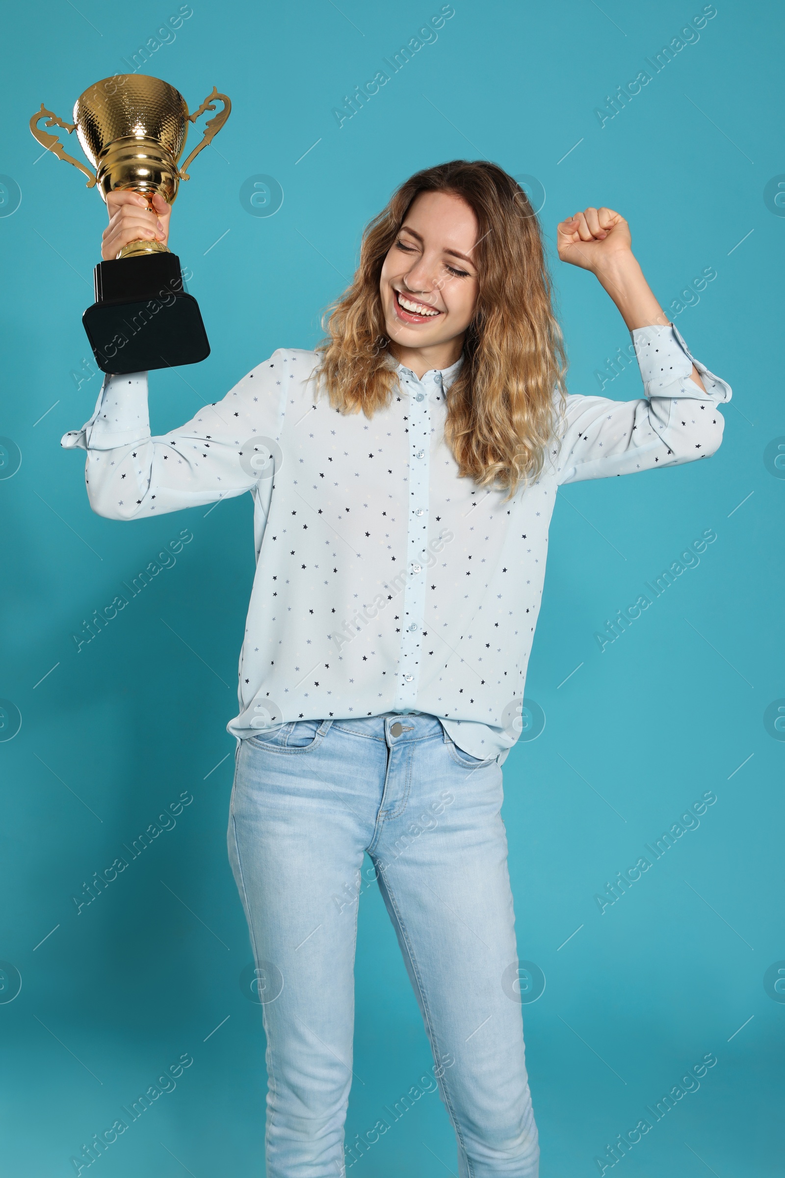 Photo of Portrait of happy young woman with gold trophy cup on blue background