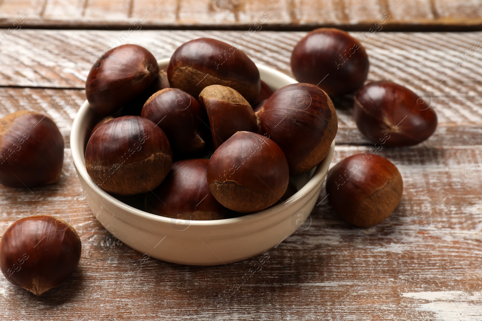 Photo of Sweet fresh edible chestnuts in bowl on wooden table, closeup