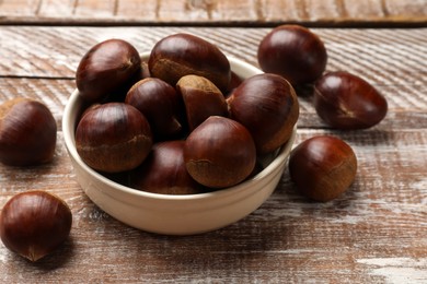 Sweet fresh edible chestnuts in bowl on wooden table, closeup