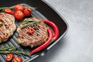 Grill pan with delicious pork steaks, spices and vegetables on grey table, closeup