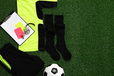 Photo of Uniform, soccer ball and other referee equipment on green grass, flat lay. Space for text