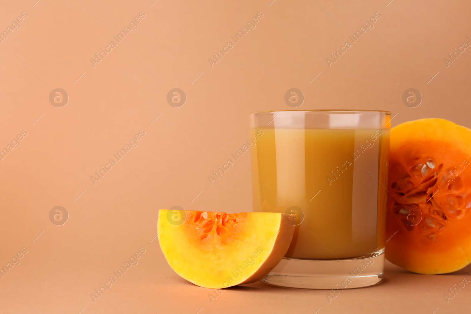 Photo of Tasty pumpkin juice in glass and cut pumpkin on pale orange background. Space for text