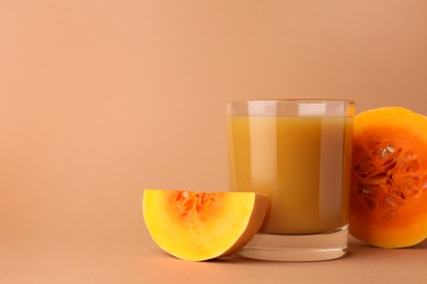 Tasty pumpkin juice in glass and cut pumpkin on pale orange background. Space for text
