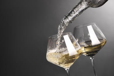 Pouring white wine into glass against grey background, closeup. Space for text