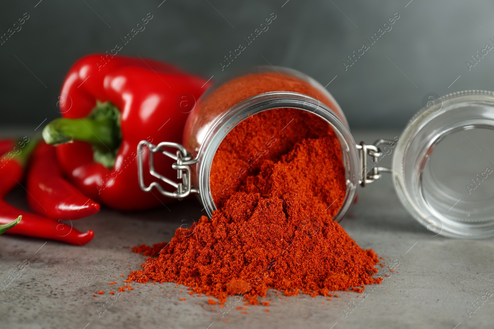Photo of Glass jar of paprika with red peppers on light grey table, closeup