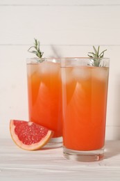 Photo of Tasty grapefruit drink with ice and rosemary in glasses on white wooden table