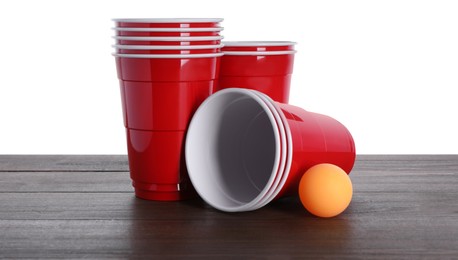 Photo of Plastic cups and ball for beer pong on wooden table against white background