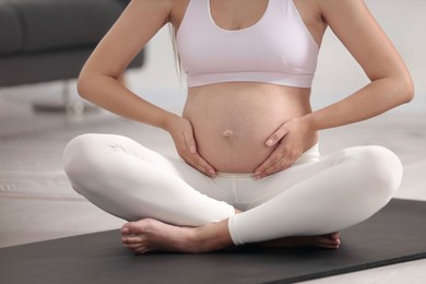 Photo of Pregnant woman sitting on yoga mat at home, closeup