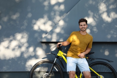 Photo of Handsome young man with bicycle near grey wall on city street. Space for text
