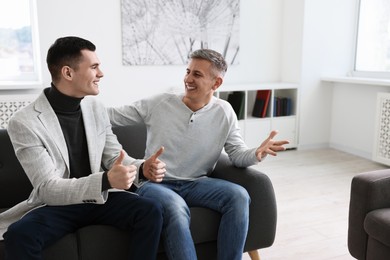 Photo of Happy men talking while sitting on sofa at home