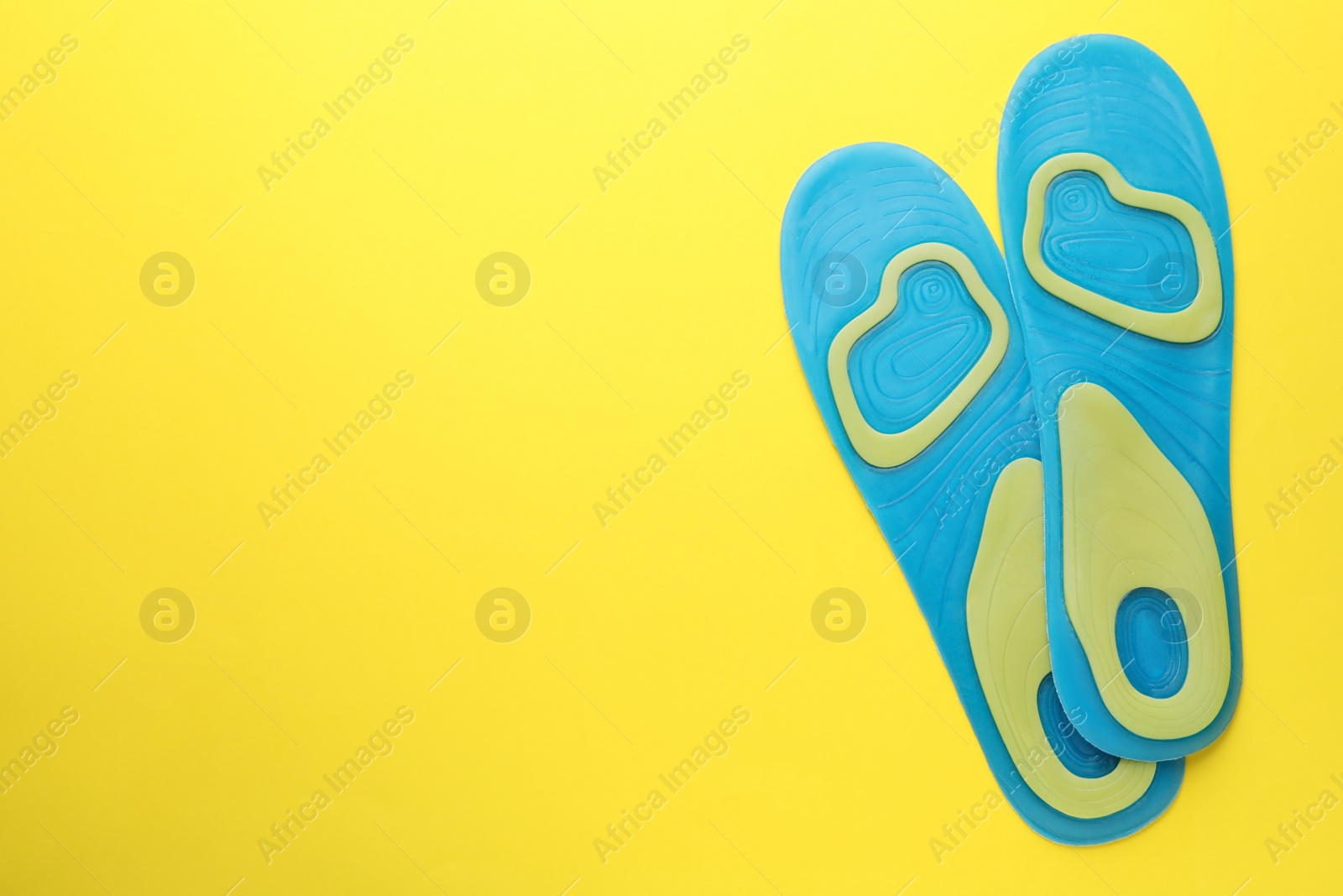 Photo of LIght blue orthopedic insoles on yellow background, flat lay. Space for text