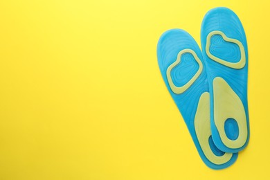 Photo of LIght blue orthopedic insoles on yellow background, flat lay. Space for text
