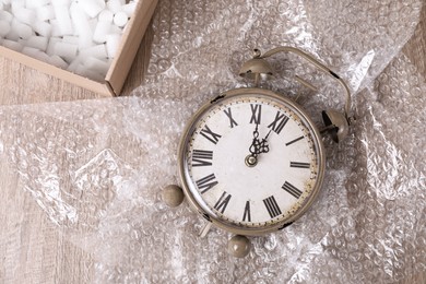 Vintage alarm clock, bubble wrap and box with packaging foam on wooden table, flat lay