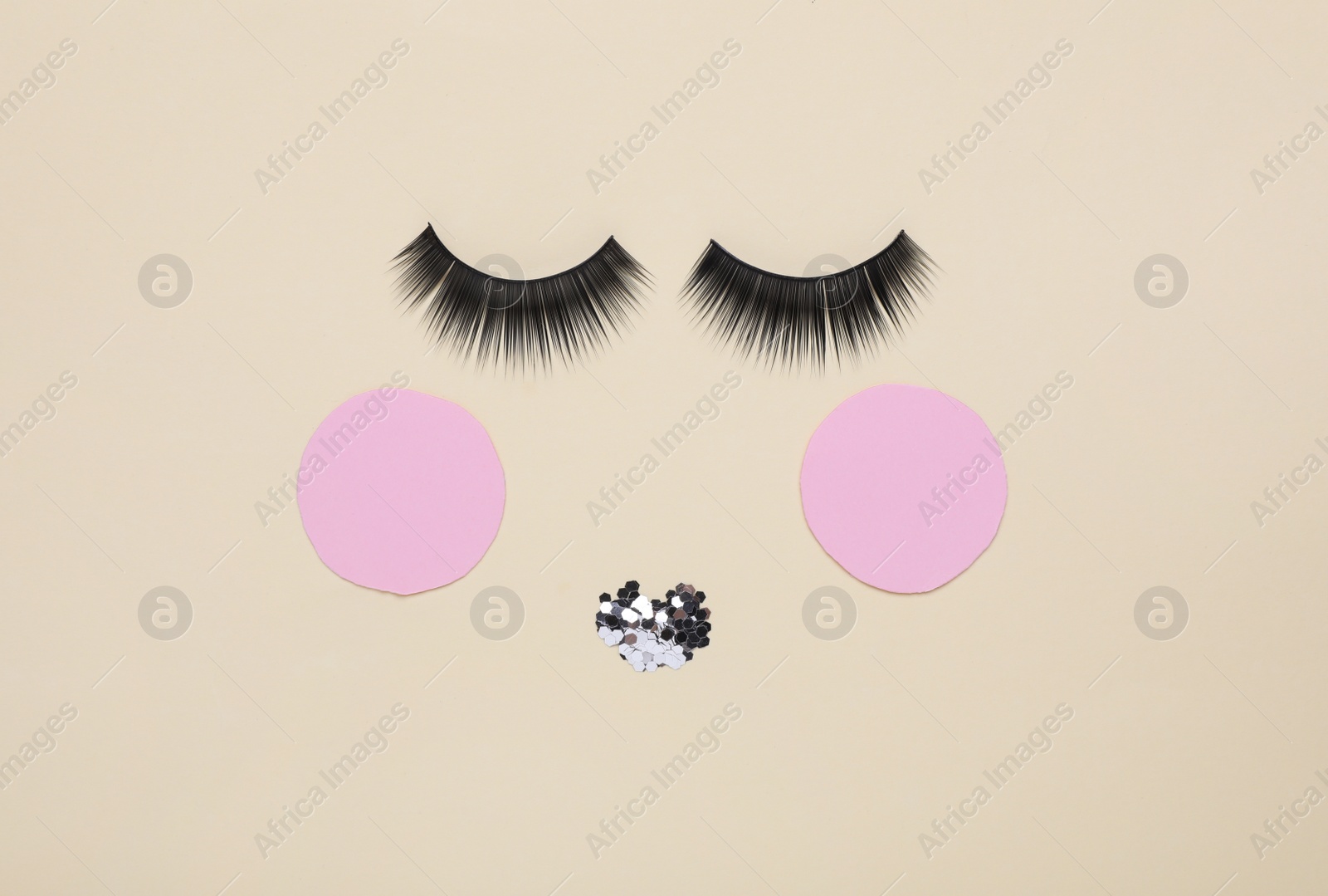 Photo of False eyelashes, pink paper circles and sequins as beautiful face on beige background, flat lay