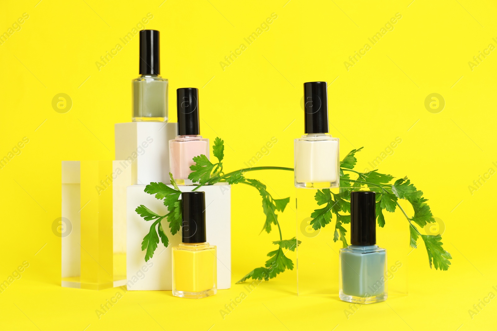 Photo of Stylish presentation of beautiful nail polishes in bottles on yellow background