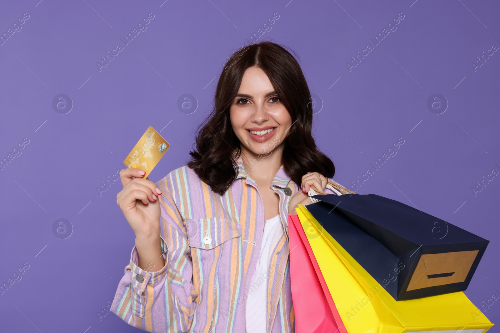 Photo of Beautiful young woman with paper shopping bags and credit card on purple background