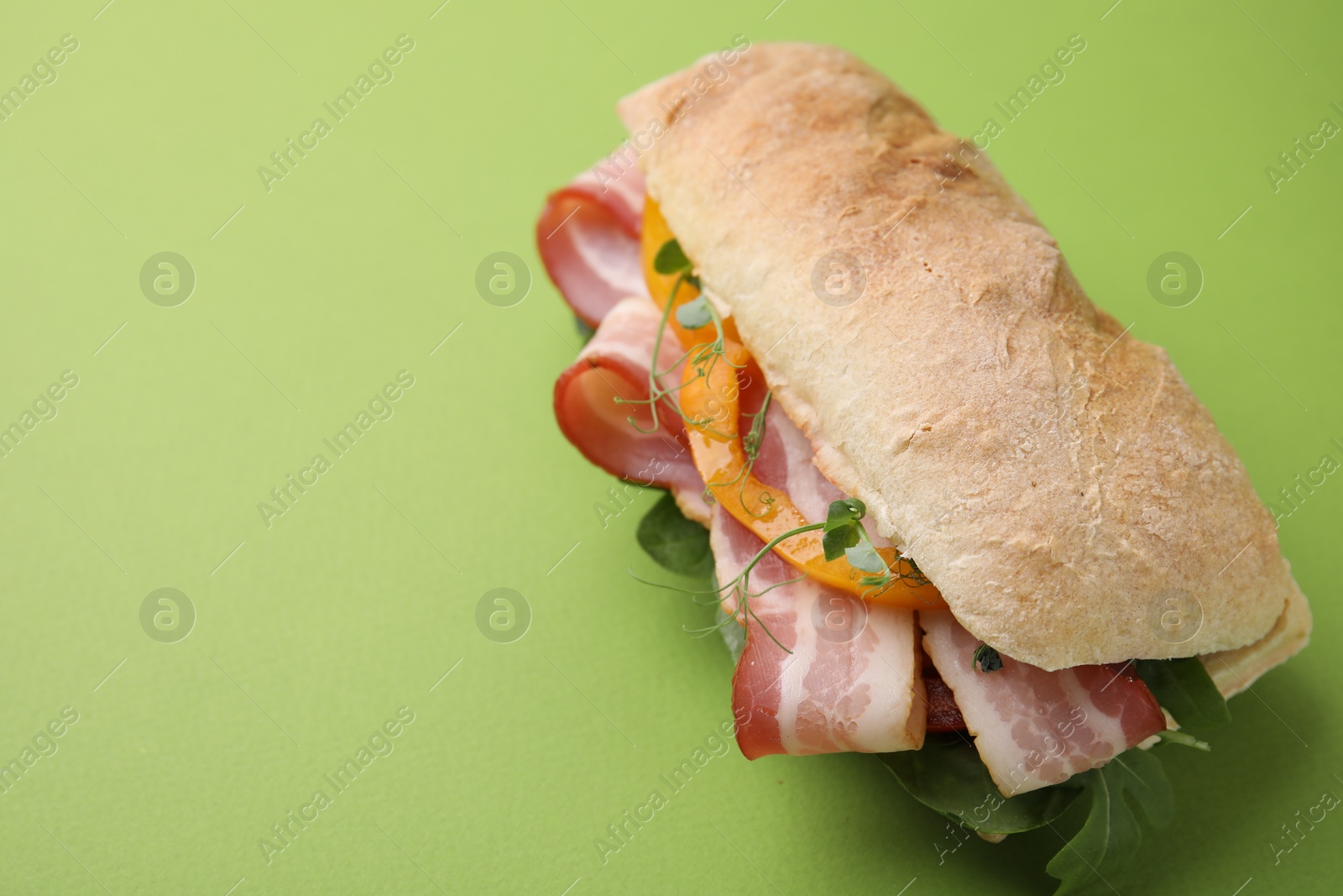 Photo of Tasty sandwich with bacon and bell pepper on green table, space for text