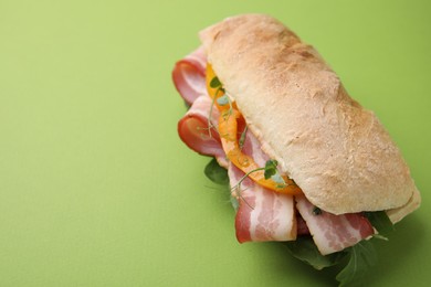 Photo of Tasty sandwich with bacon and bell pepper on green table, space for text