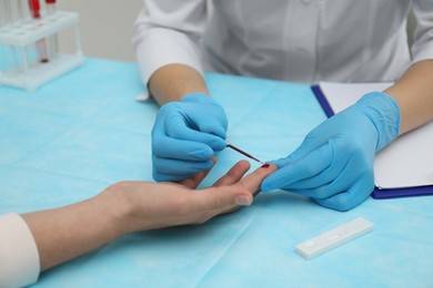 Doctor taking blood sample from patient's finger at table, closeup