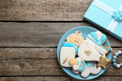 Photo of Cute tasty cookies of different shapes, gift box and space for text on wooden table. Baby shower party