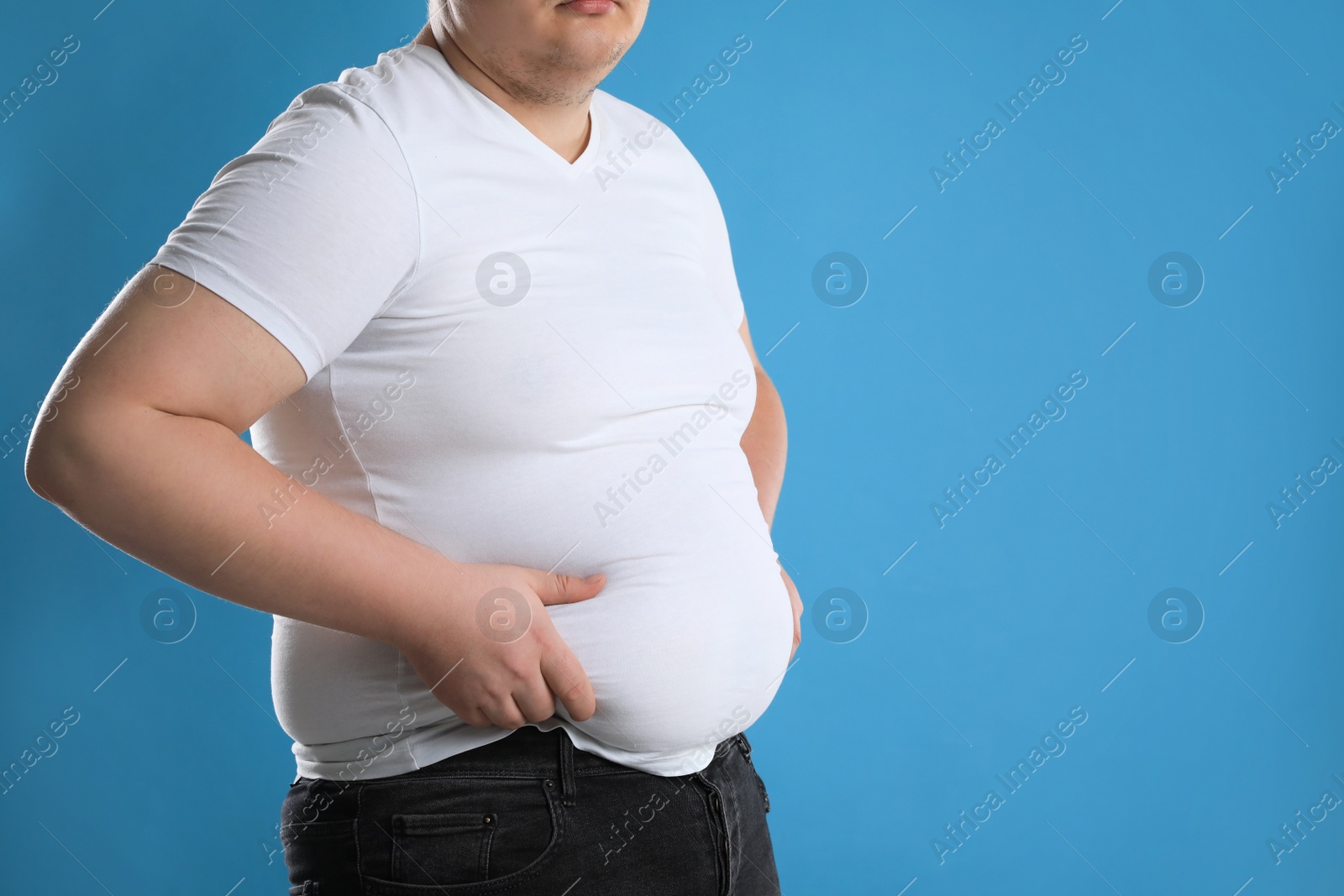 Photo of Overweight man in tight t-shirt on light blue background, closeup. Space for text
