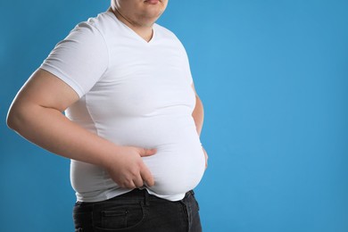 Photo of Overweight man in tight t-shirt on light blue background, closeup. Space for text