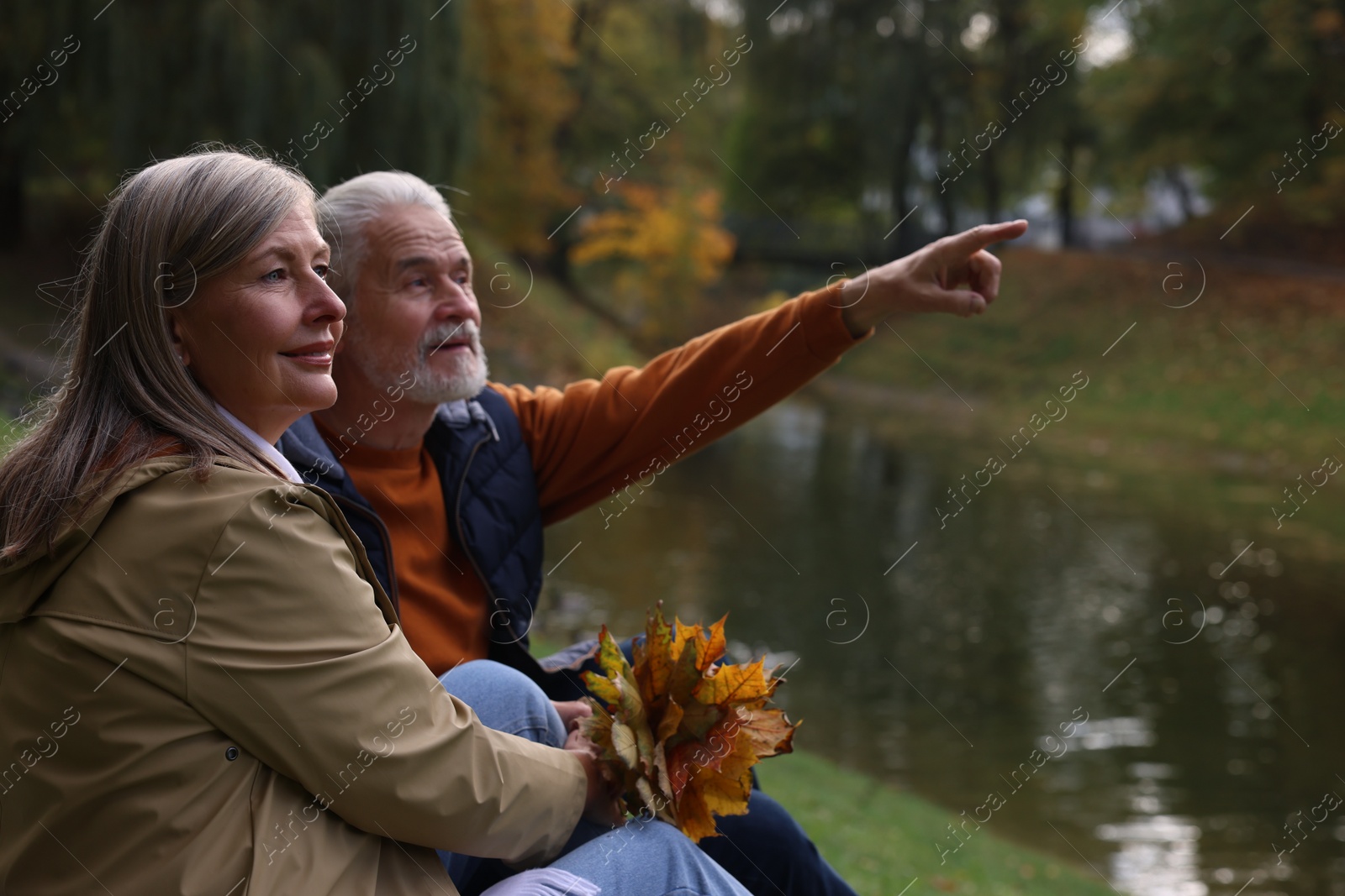 Photo of Affectionate senior couple with dry leaves near river in autumn park