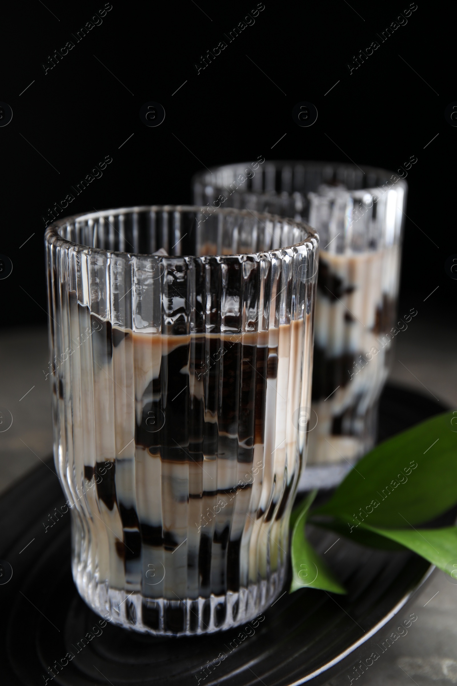 Photo of Glasses of milk with grass jelly and green leaves on grey table, closeup