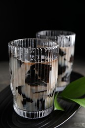 Photo of Glasses of milk with grass jelly and green leaves on grey table, closeup