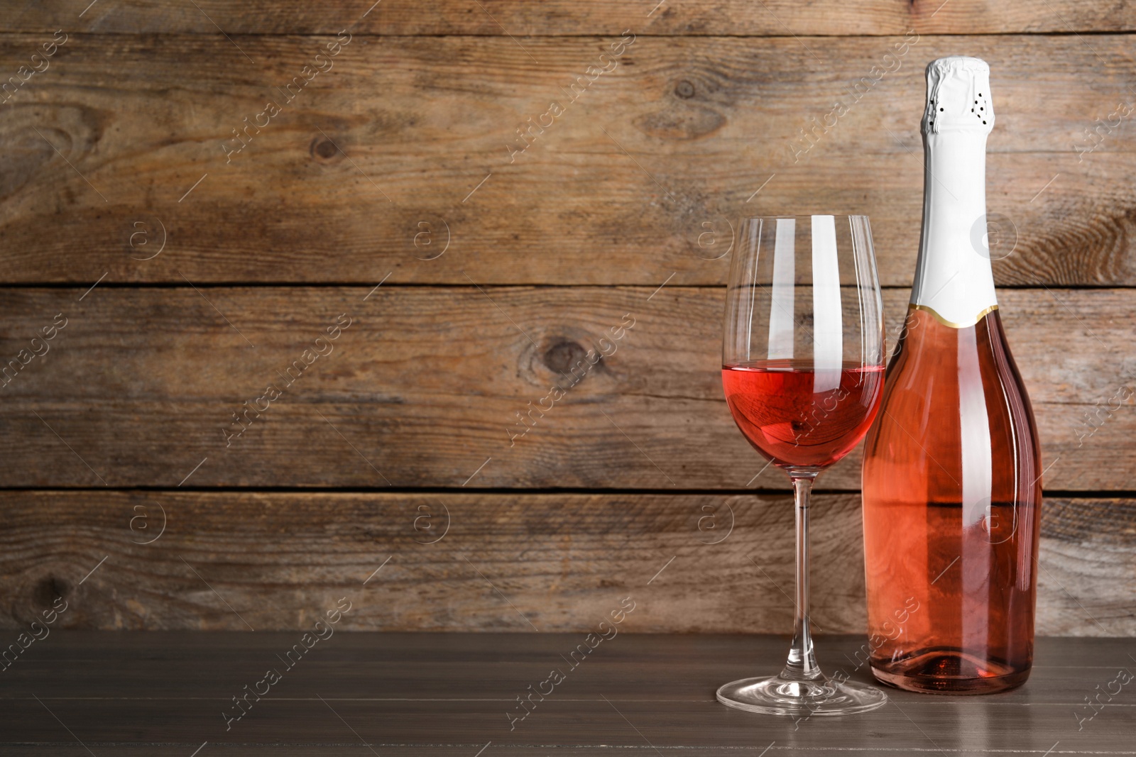 Photo of Bottle and glass of delicious rose wine on table against wooden background. Space for text