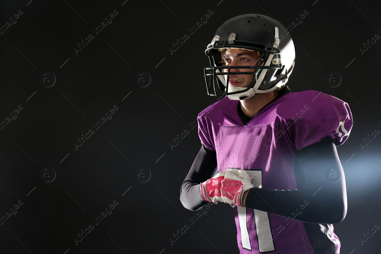 Photo of American football player wearing uniform on dark background. Space for text