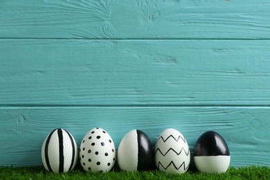 Line of painted Easter eggs on green lawn against wooden background, space for text